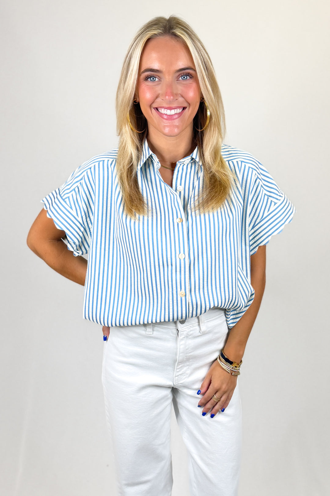 Woman wearing a blue and white striped shirt and white pants on a plain background