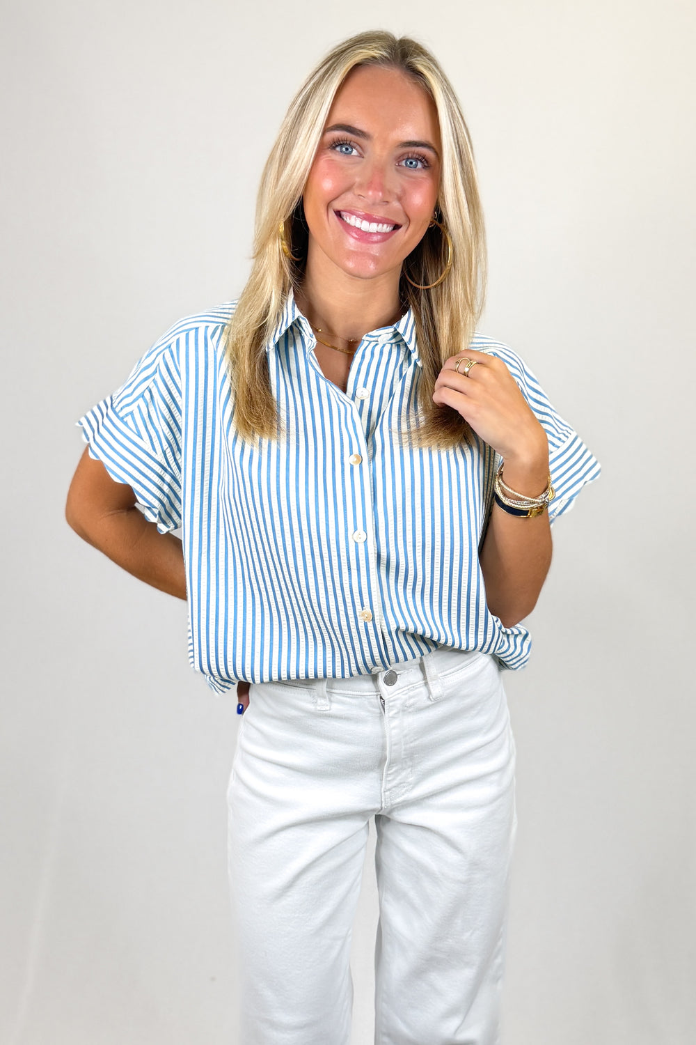 Woman wearing a blue and white striped shirt and white pants against a plain background