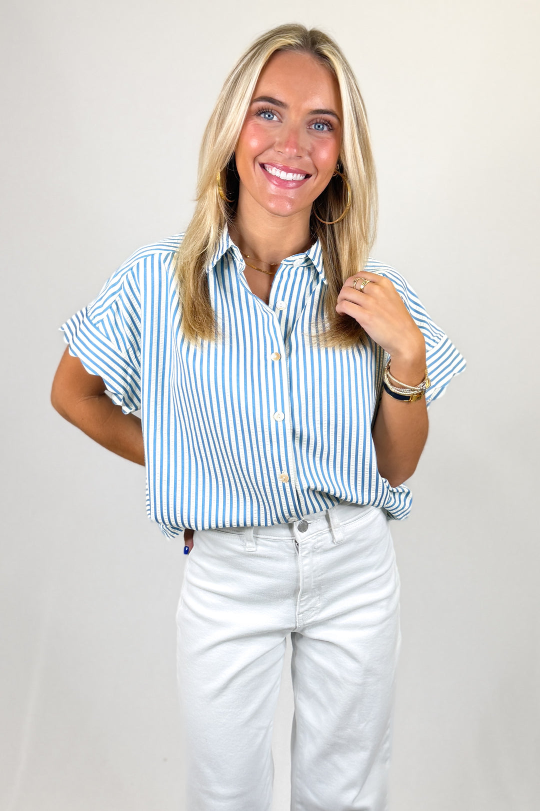 Woman wearing a blue and white striped shirt and white pants against a plain background