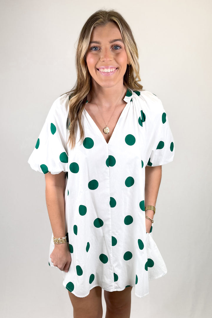 Woman wearing a white dress with green polka dots against a plain background