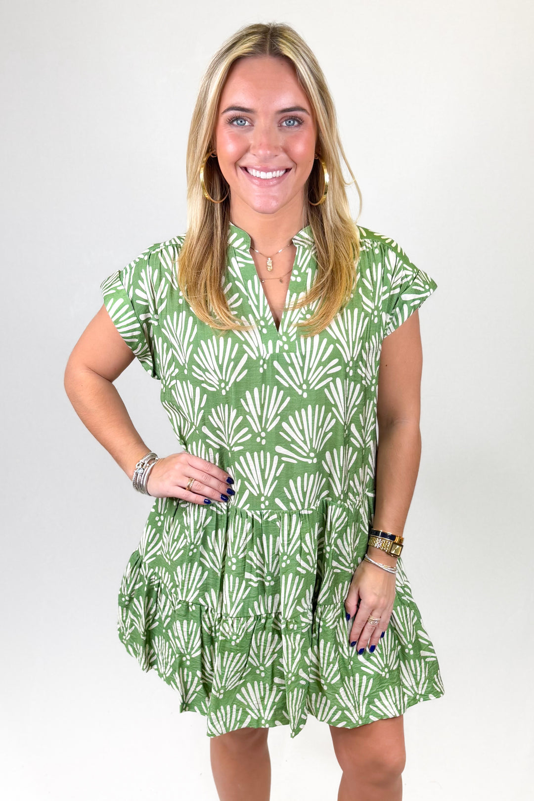 Woman wearing a green dress with white shell pattern on a plain background
