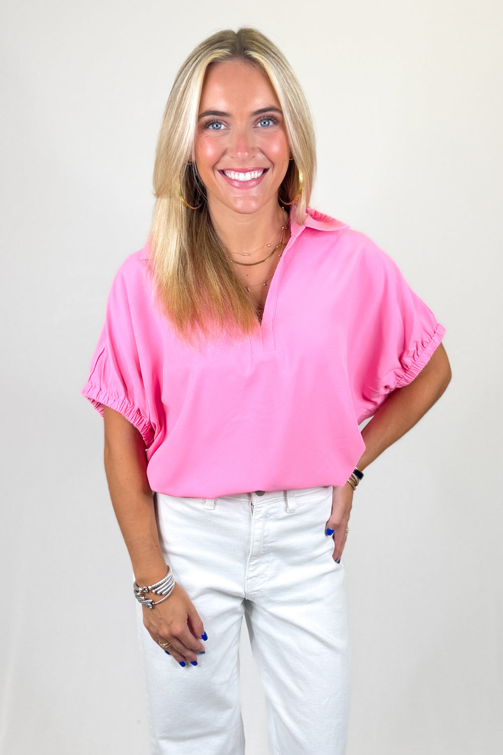 Woman wearing a pink blouse and white pants against a plain background
