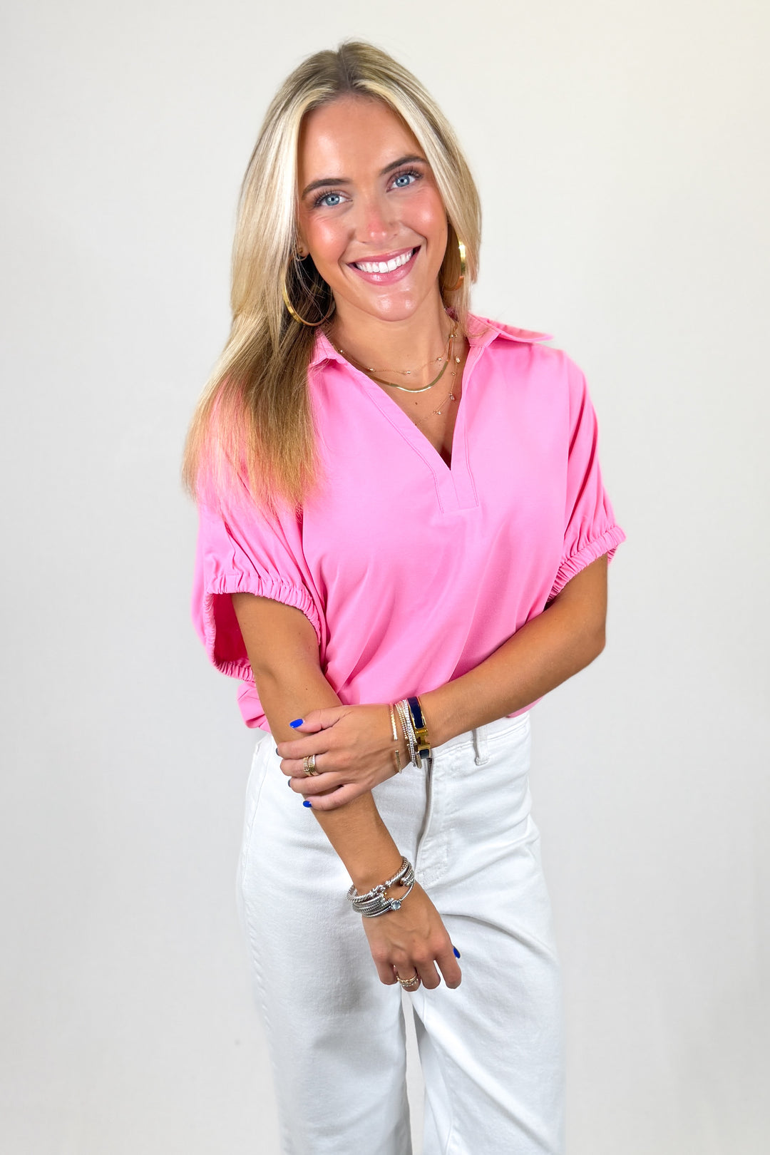 Woman wearing a pink blouse and white pants against a plain background