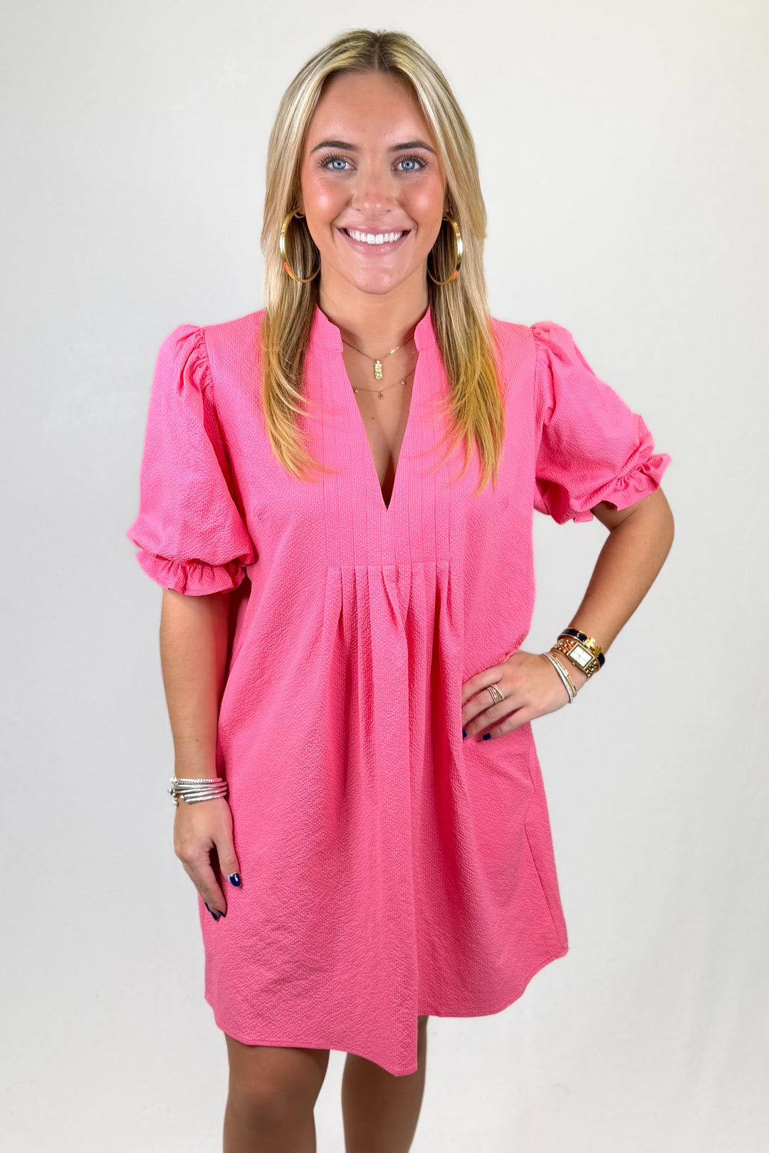 Woman wearing a bright pink dress with puff sleeves on a plain background