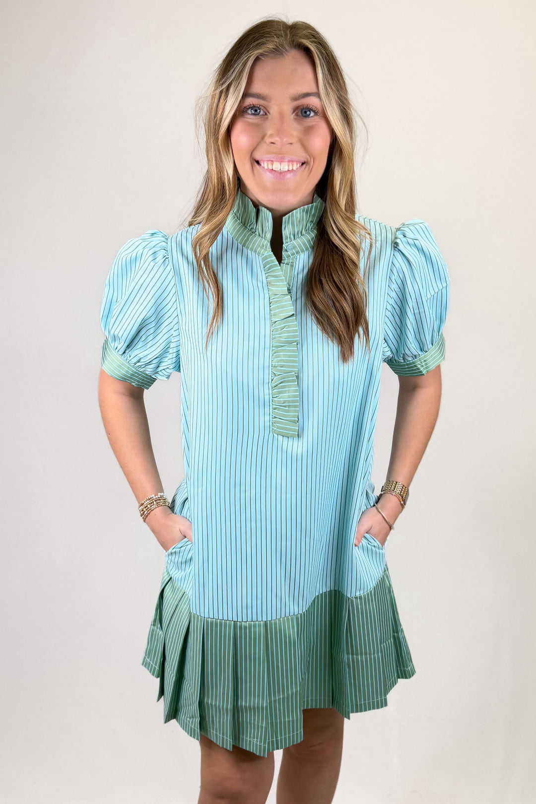 Woman wearing a light blue and green dress with puffed sleeves on a plain background