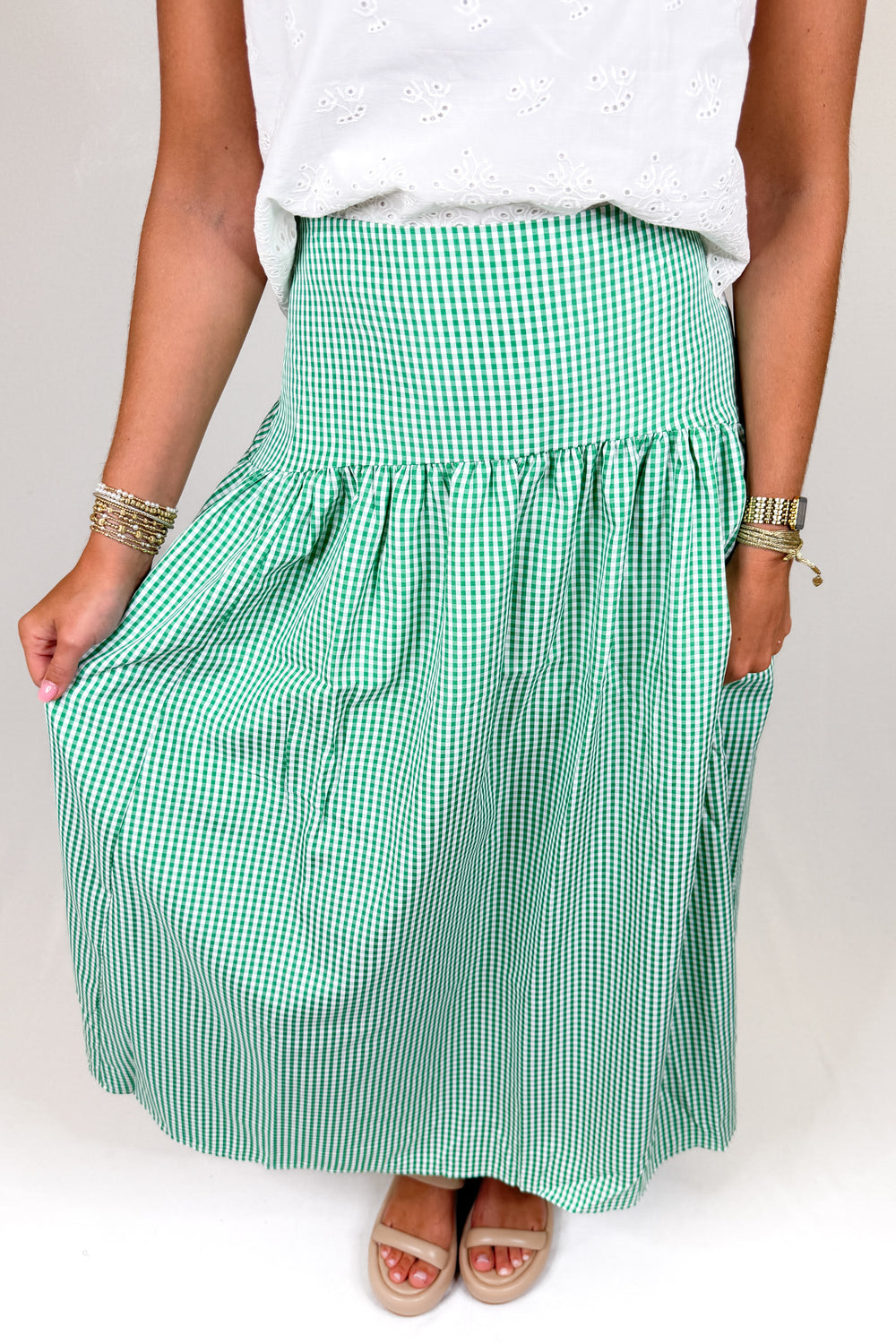 Person wearing a green gingham skirt and white top on a plain background