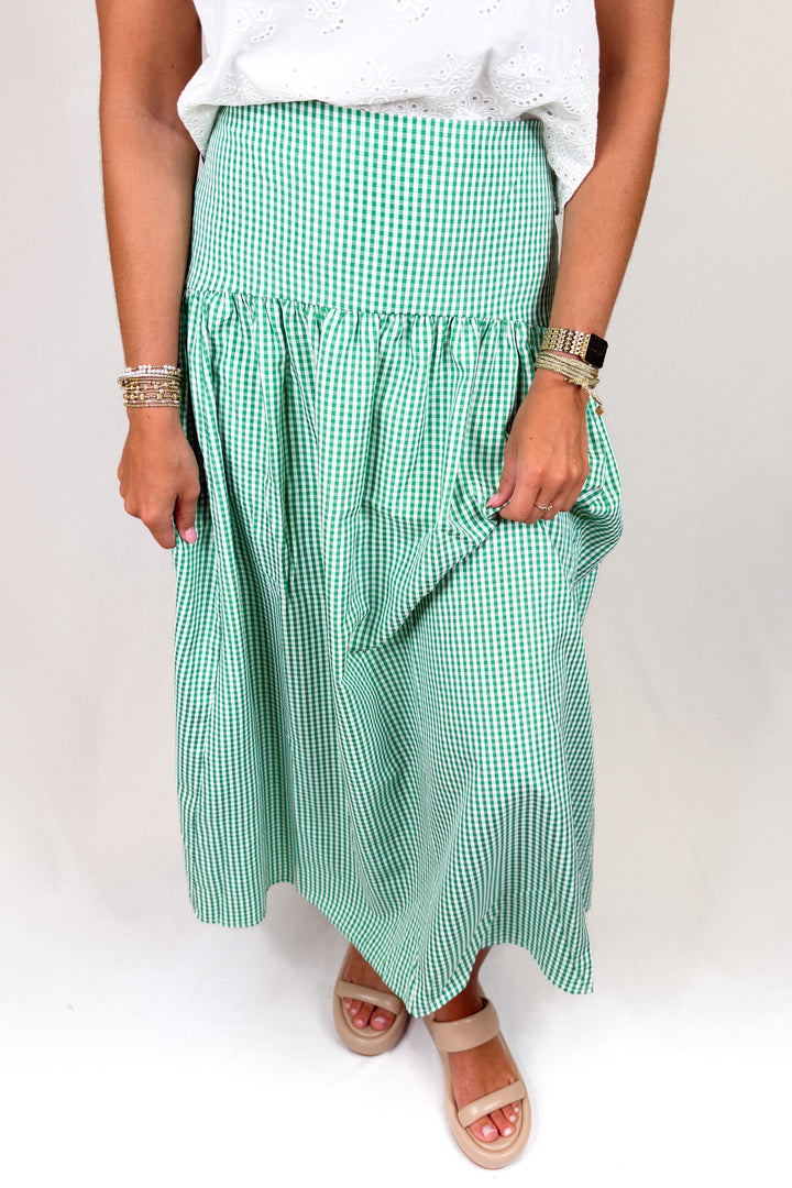 Person wearing a green gingham skirt and white top on a plain background