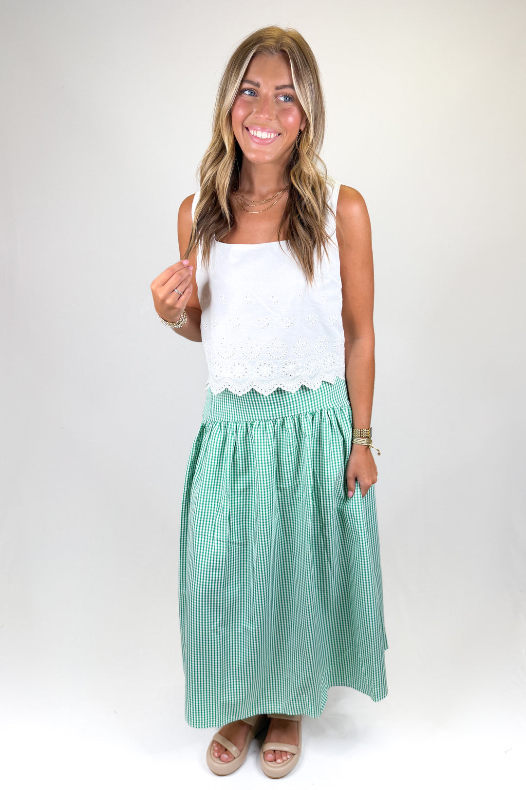 Woman wearing a white eyelet top with scalloped hem and a green checkered skirt on a plain background