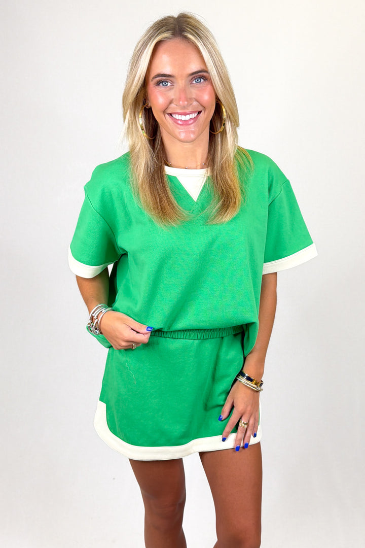 Woman wearing a green set with white trim on a plain background