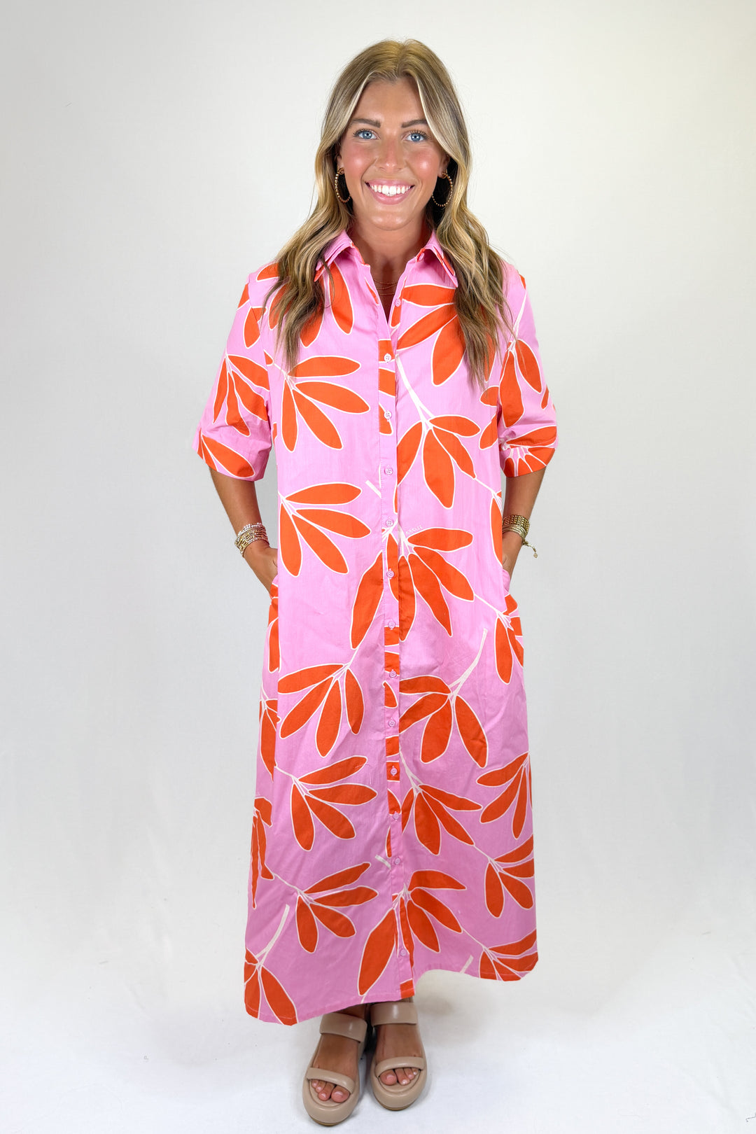 Woman wearing a pink dress with orange leaf patterns on a white background