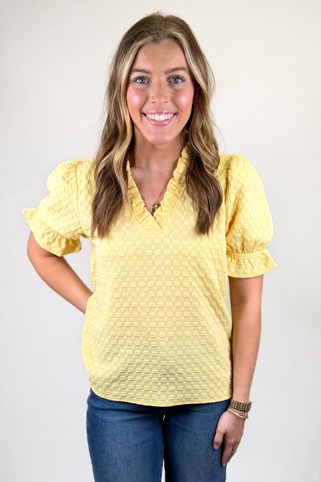 Woman wearing a yellow textured blouse with blue jeans on a white background