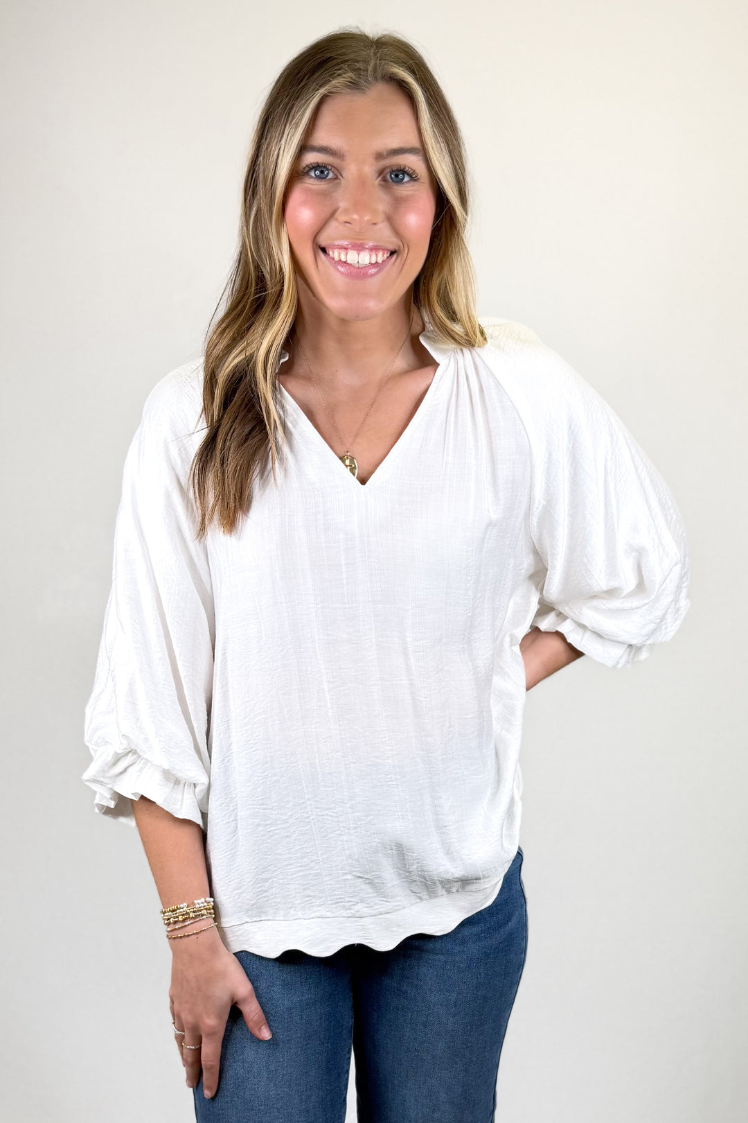 Woman wearing a white blouse and blue jeans against a plain background