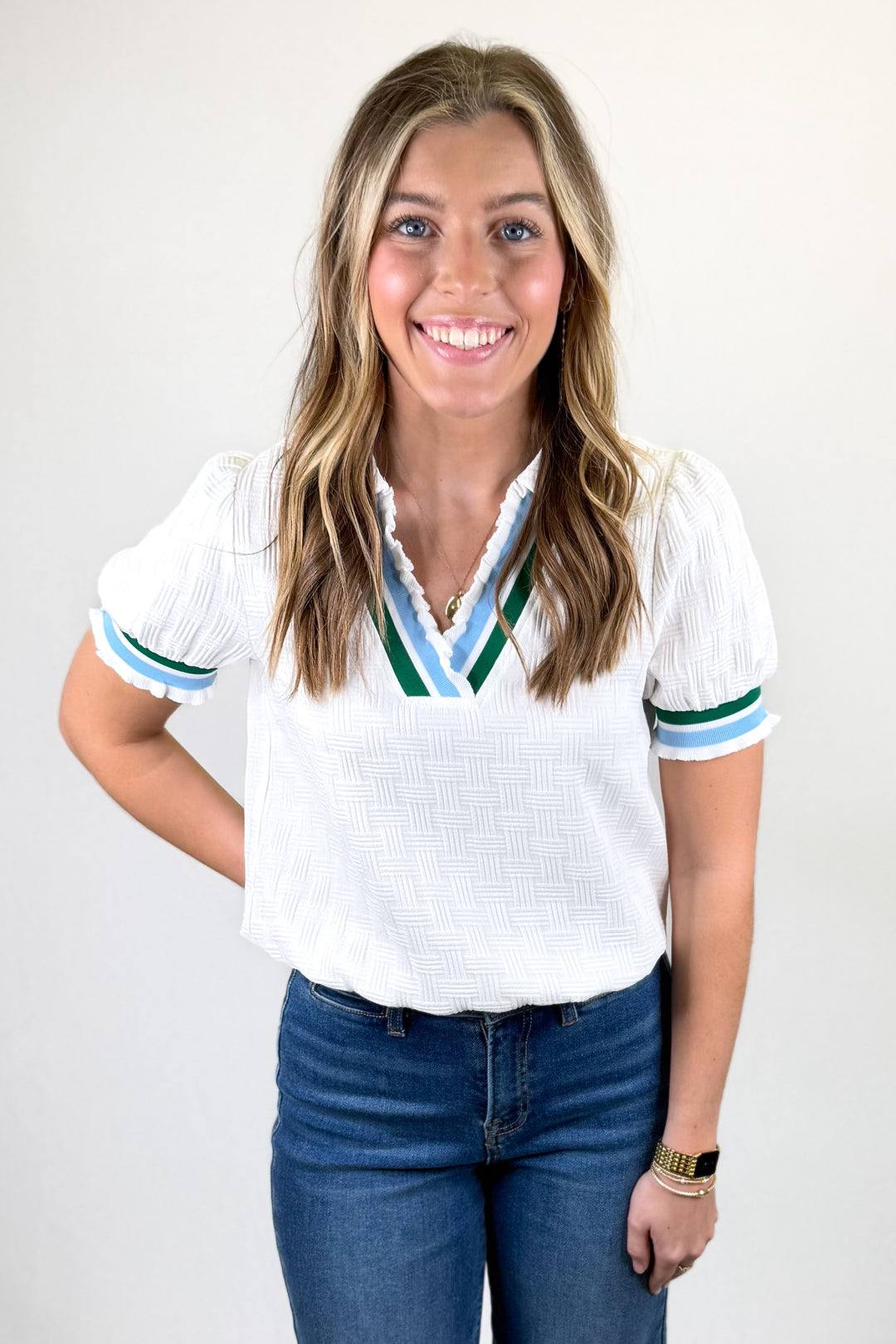Woman wearing a white blouse with colorful trim and blue jeans on a plain background