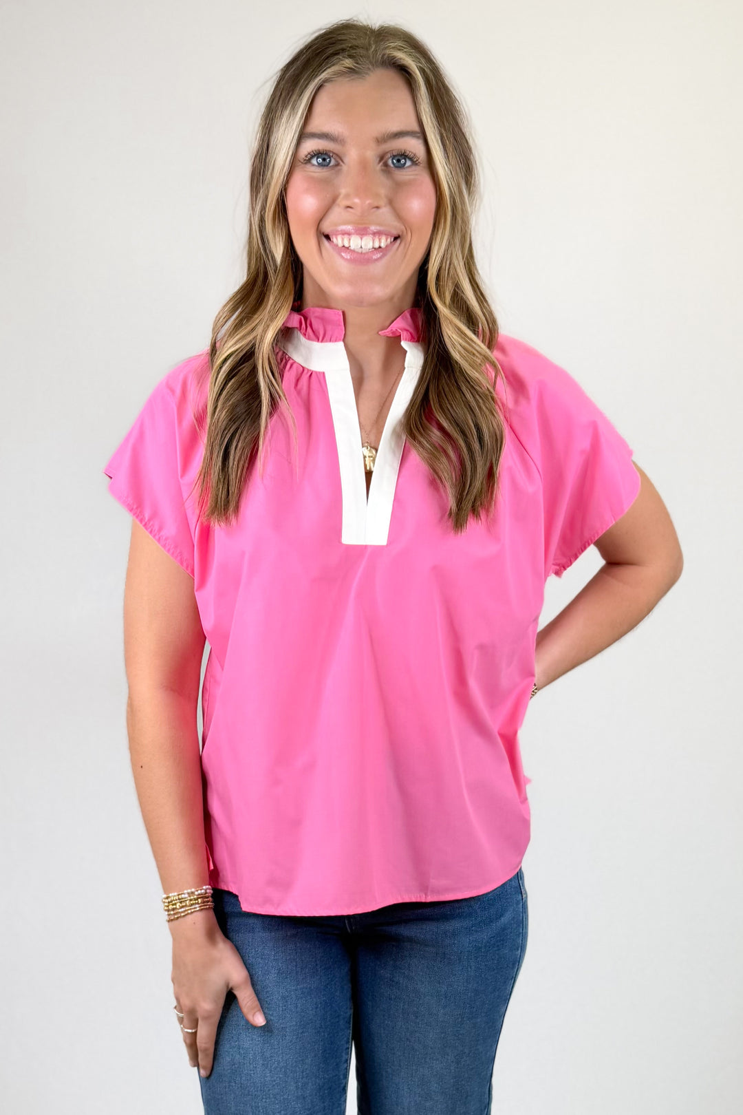 Woman wearing a pink blouse with a white collar against a plain background