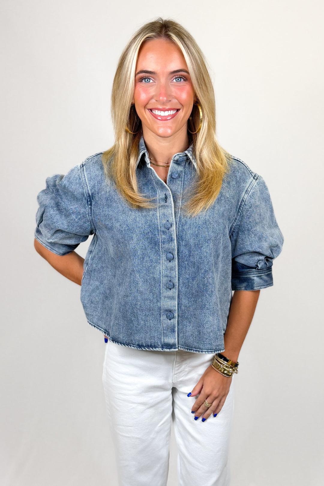 Woman wearing a denim shirt and white pants against a plain background