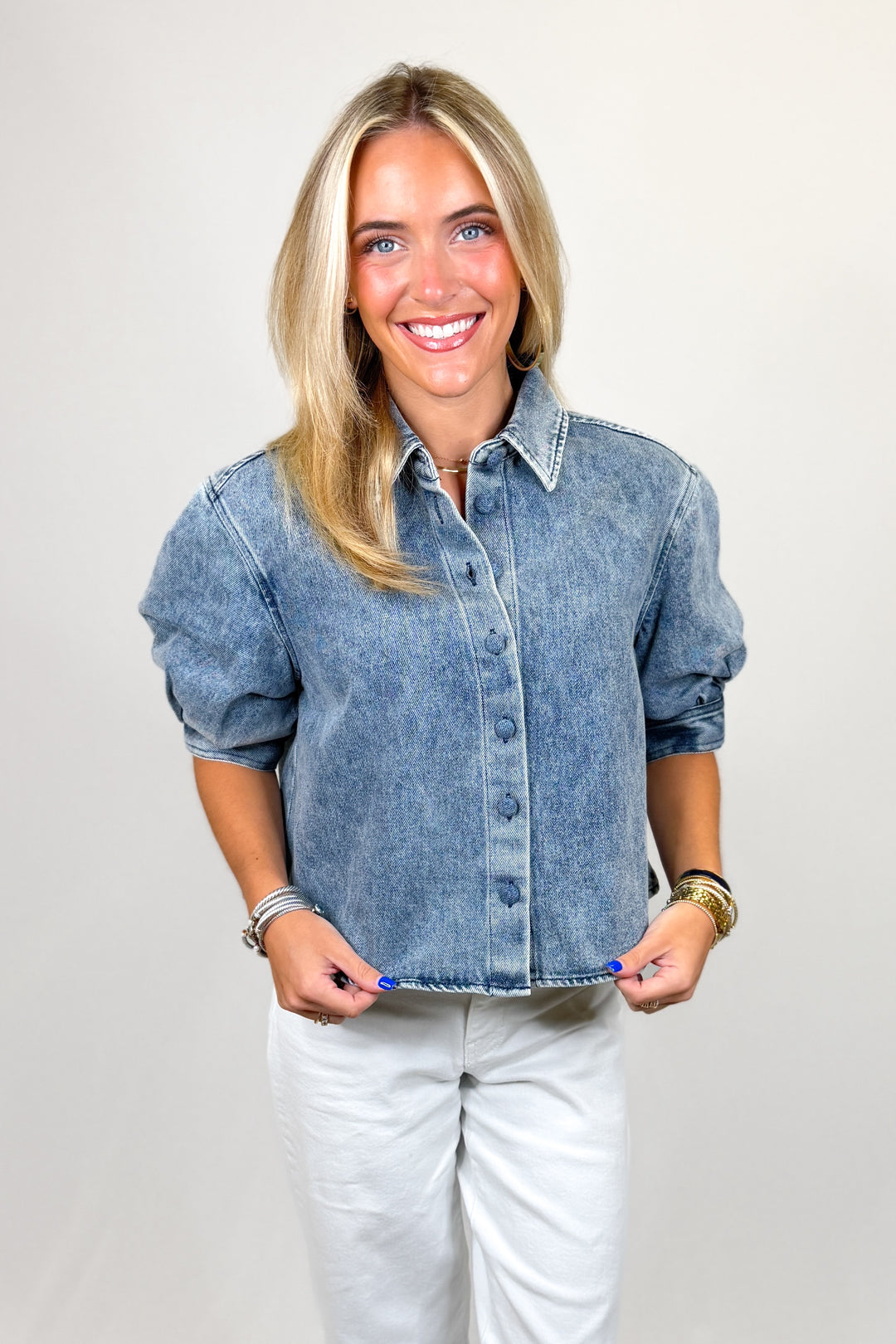 Woman wearing a denim shirt and white pants against a plain background