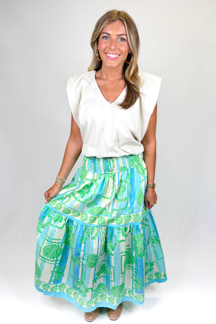 Woman wearing a white top and colorful skirt on a plain background