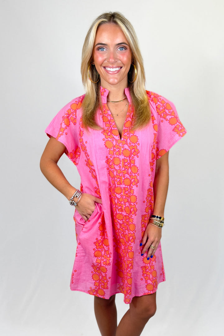 Woman wearing a pink dress with orange floral patterns on a white background
