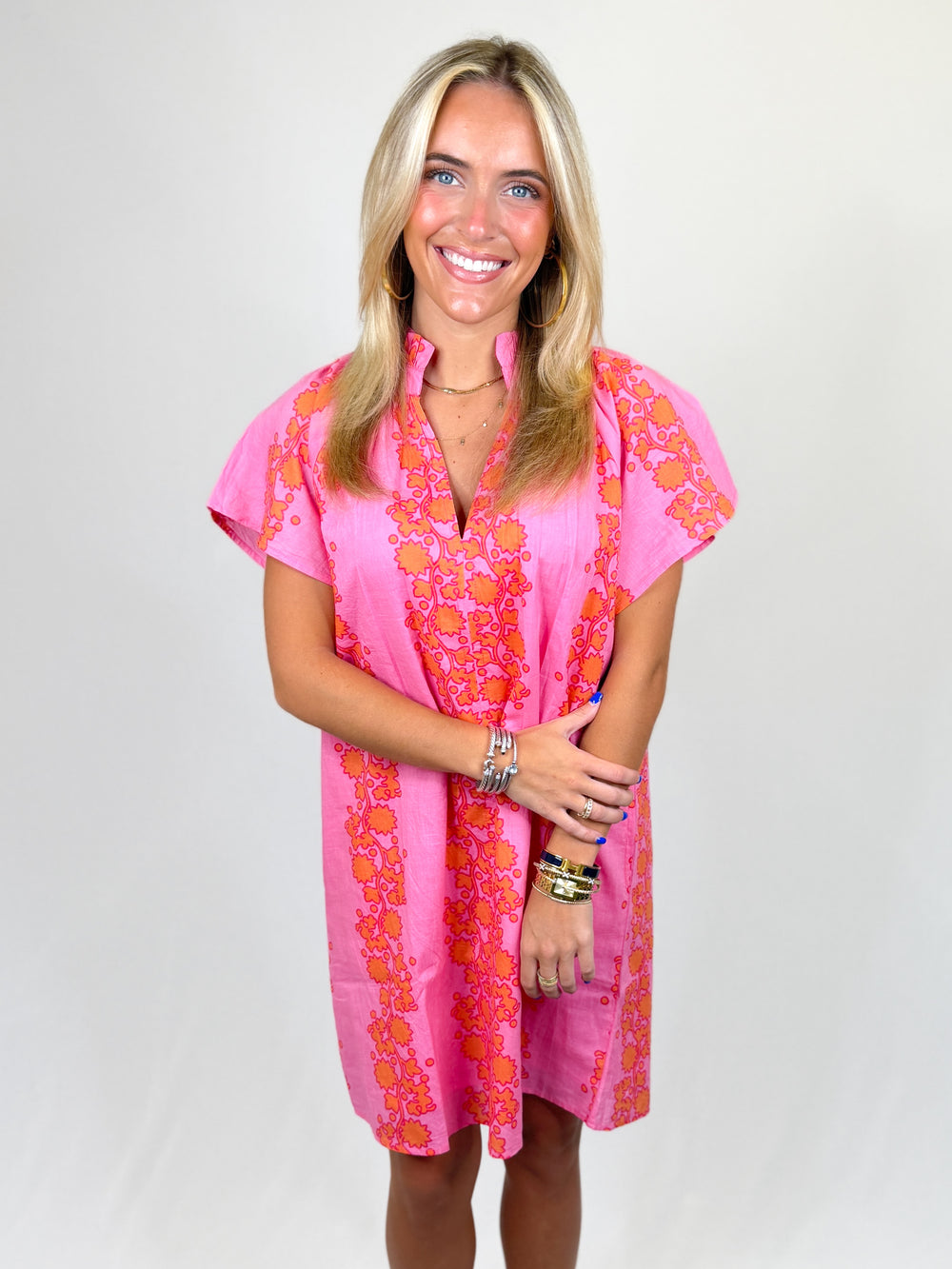 Woman wearing a pink dress with orange floral patterns on a white background