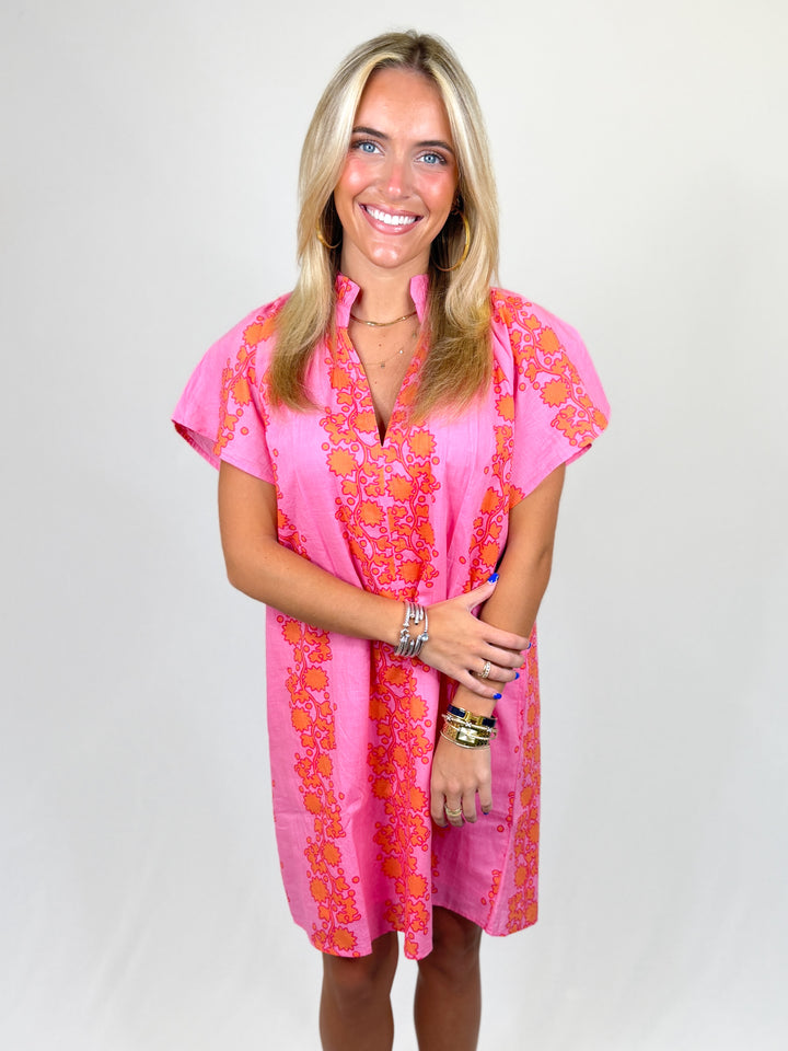 Woman wearing a pink dress with orange floral patterns on a white background