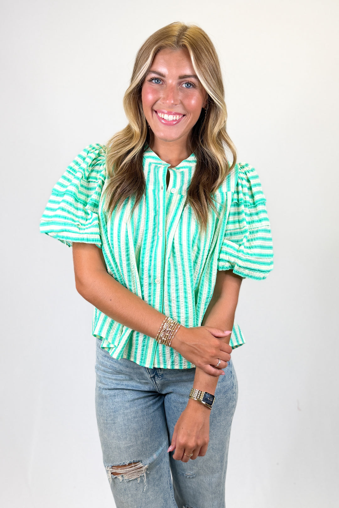 Woman wearing a green and white striped shirt with ripped jeans on a plain background