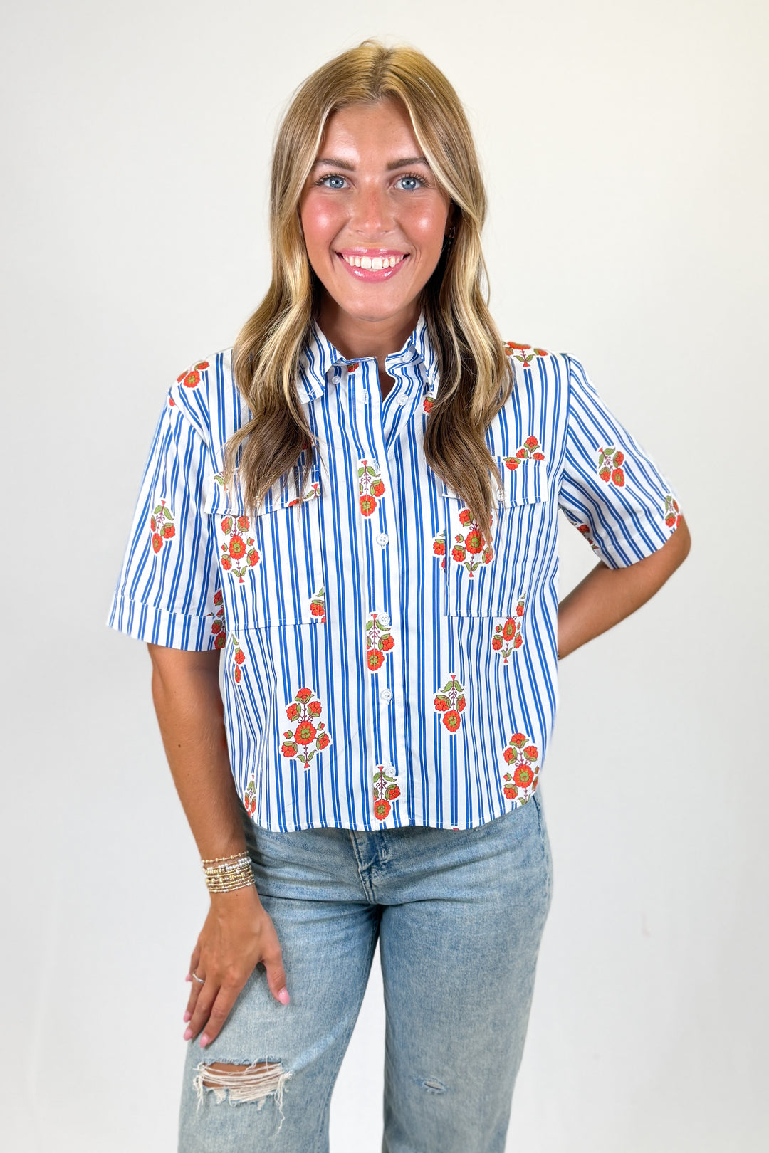 Woman wearing a blue and white striped shirt with floral patterns on a plain background