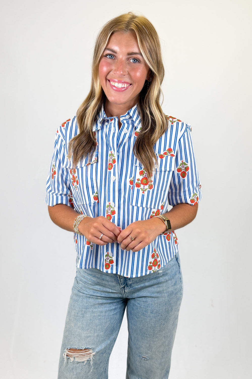 Woman wearing a blue and white striped shirt with floral patterns and jeans on a plain background