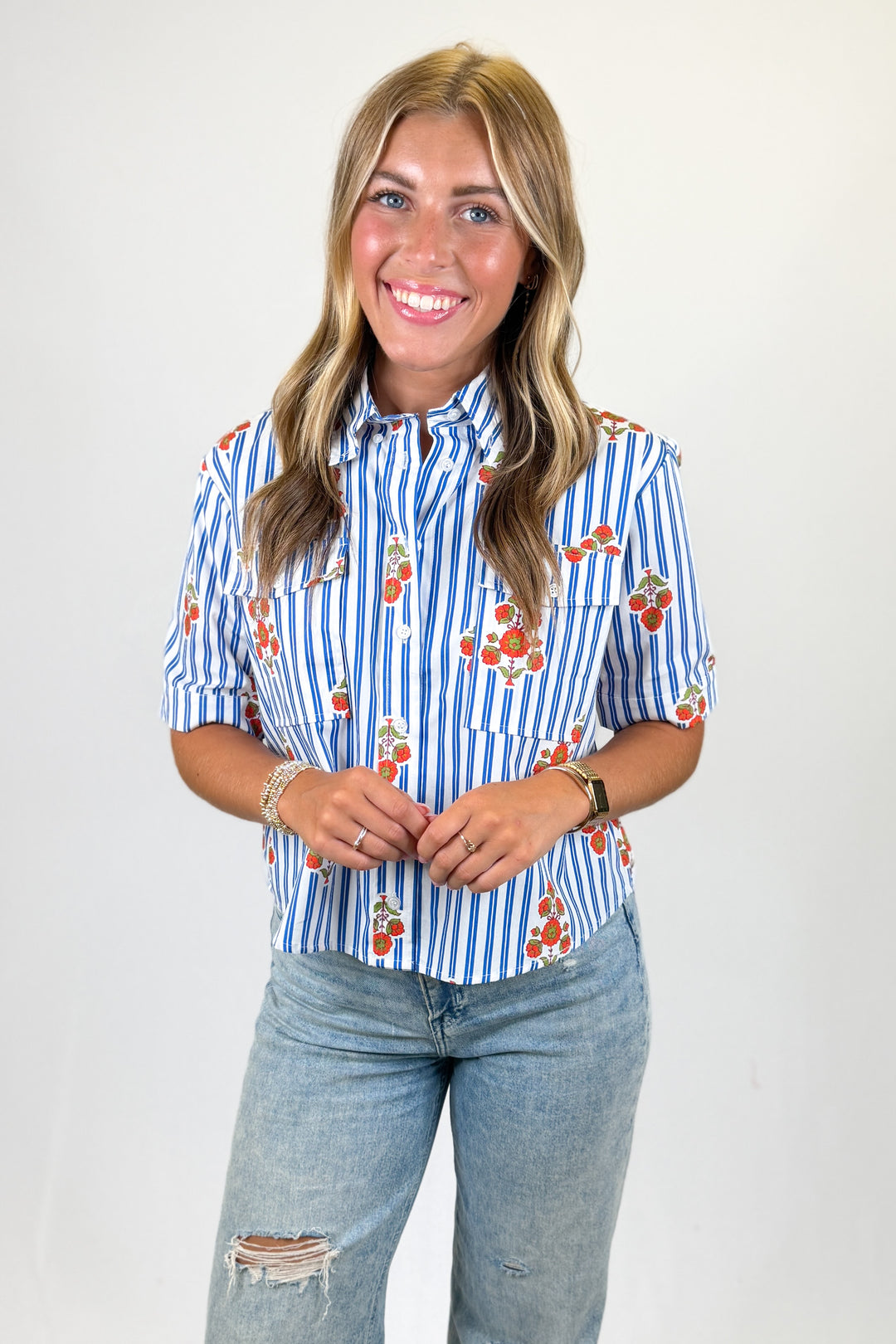 Woman wearing a blue and white striped shirt with floral patterns and jeans on a plain background