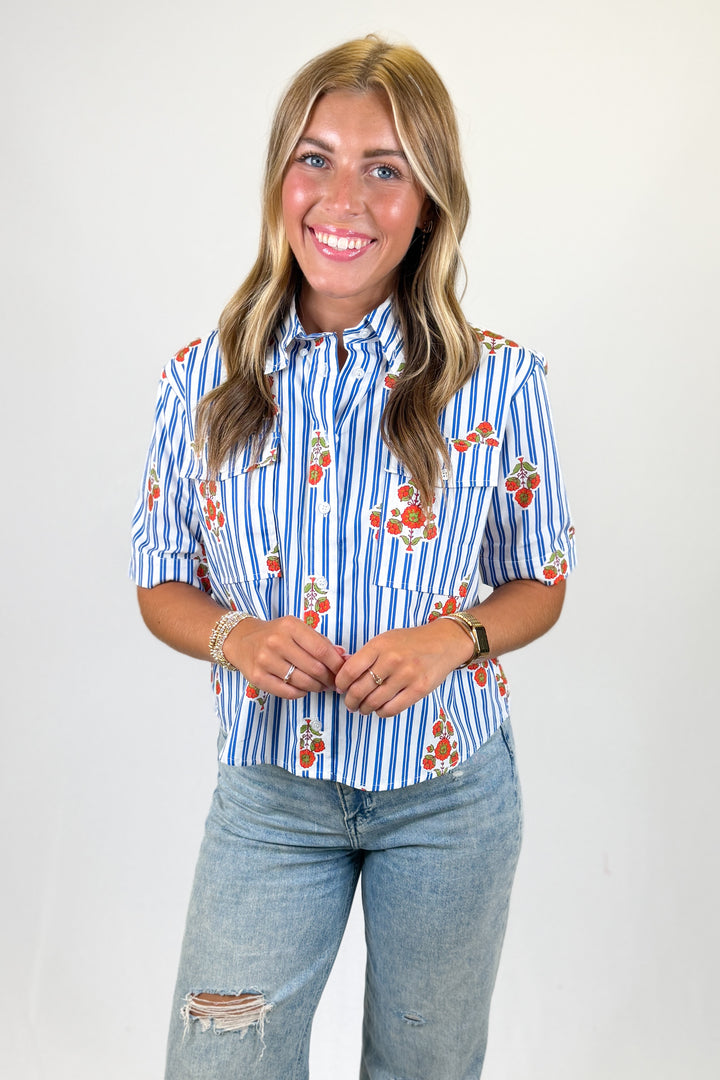 Woman wearing a blue and white striped shirt with floral patterns and jeans on a plain background