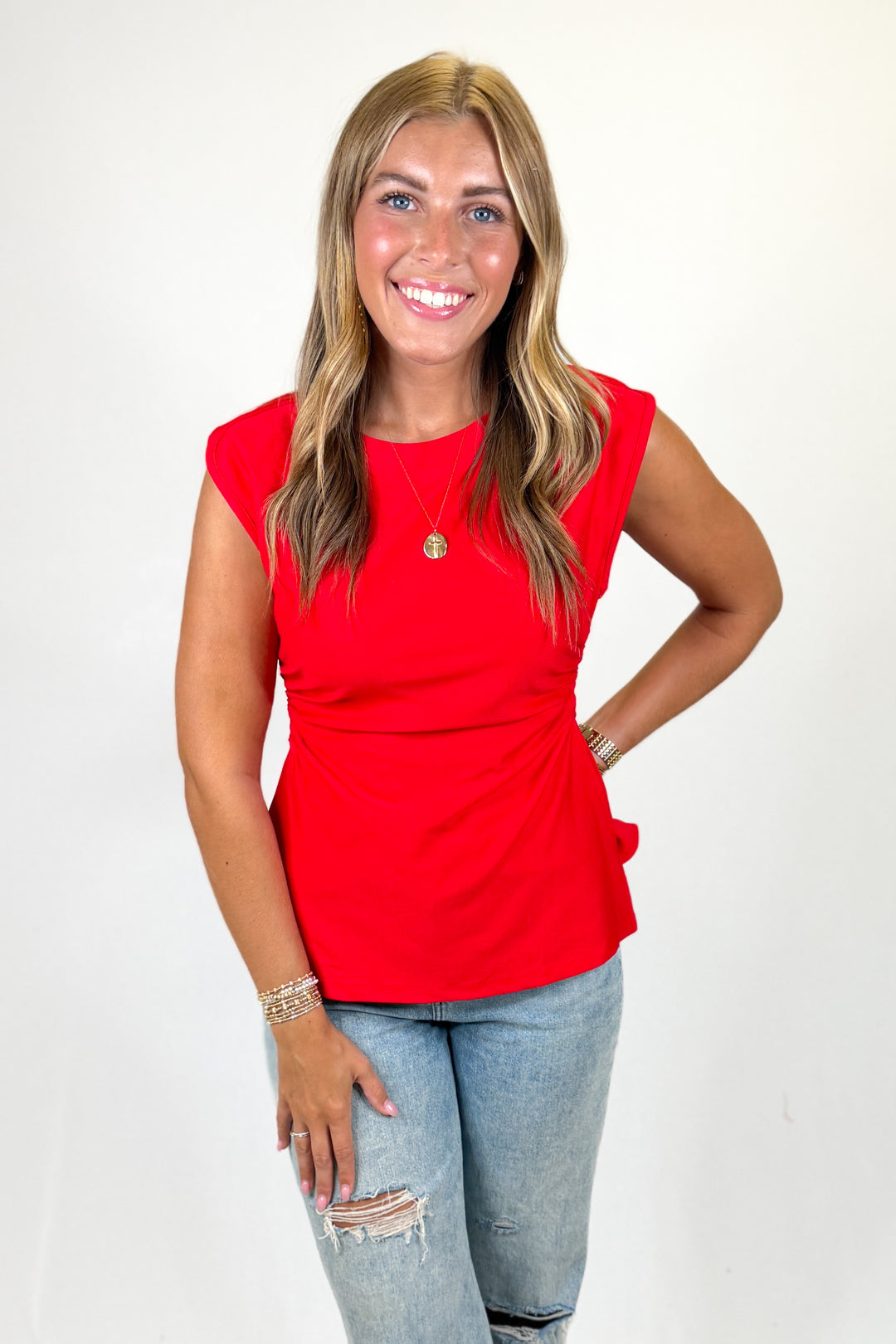 Woman wearing a red sleeveless top and light blue jeans on a white background