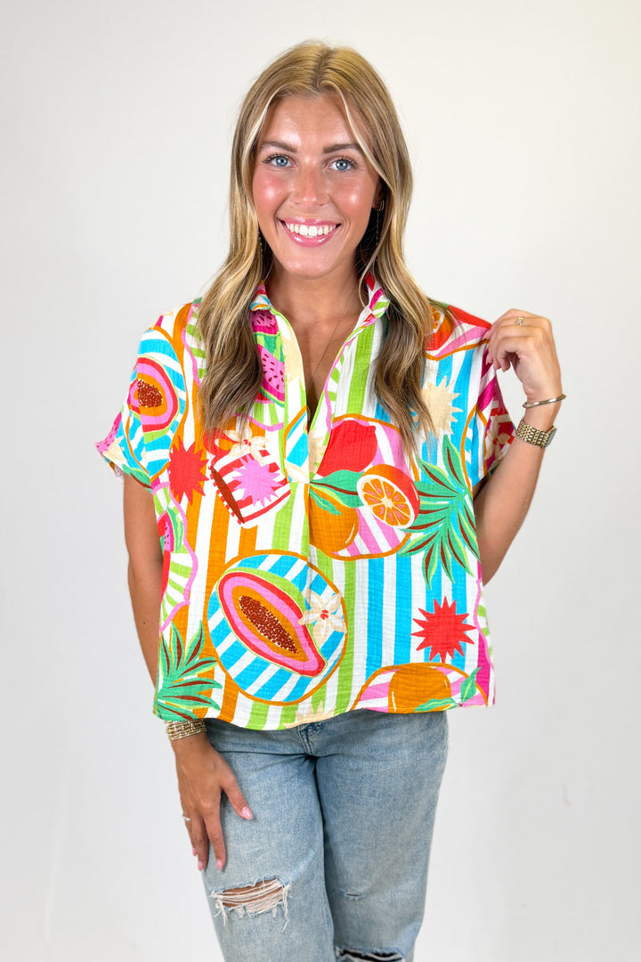 Woman wearing a colorful tropical-themed shirt with a plain background