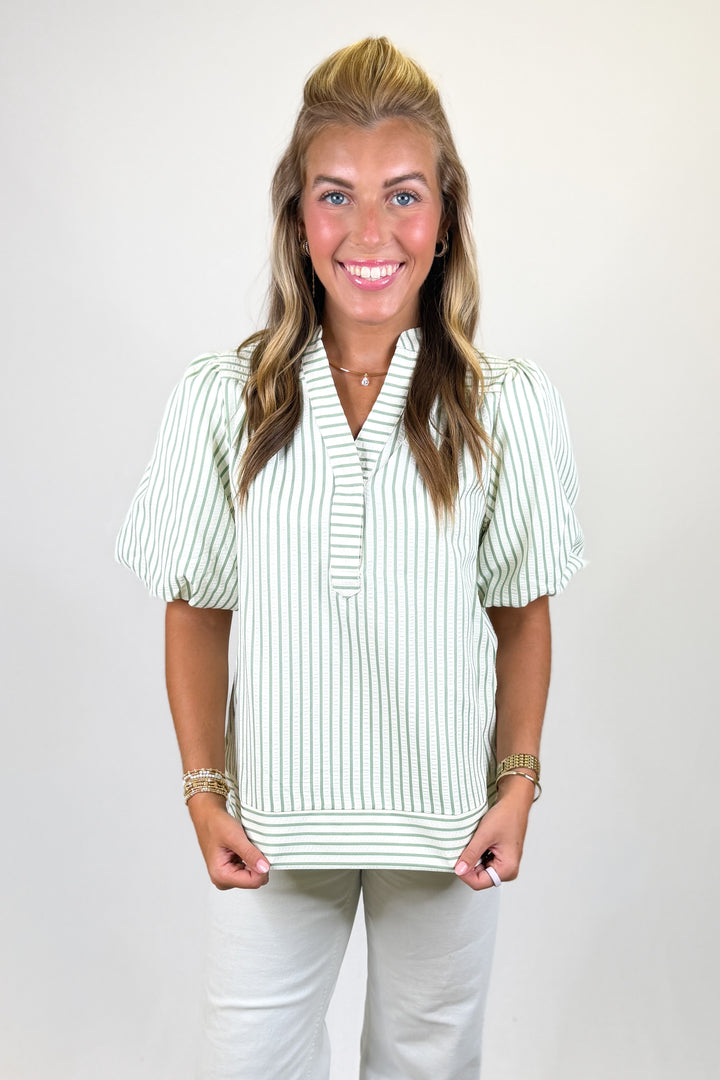 Woman wearing a striped blouse and white pants against a plain background