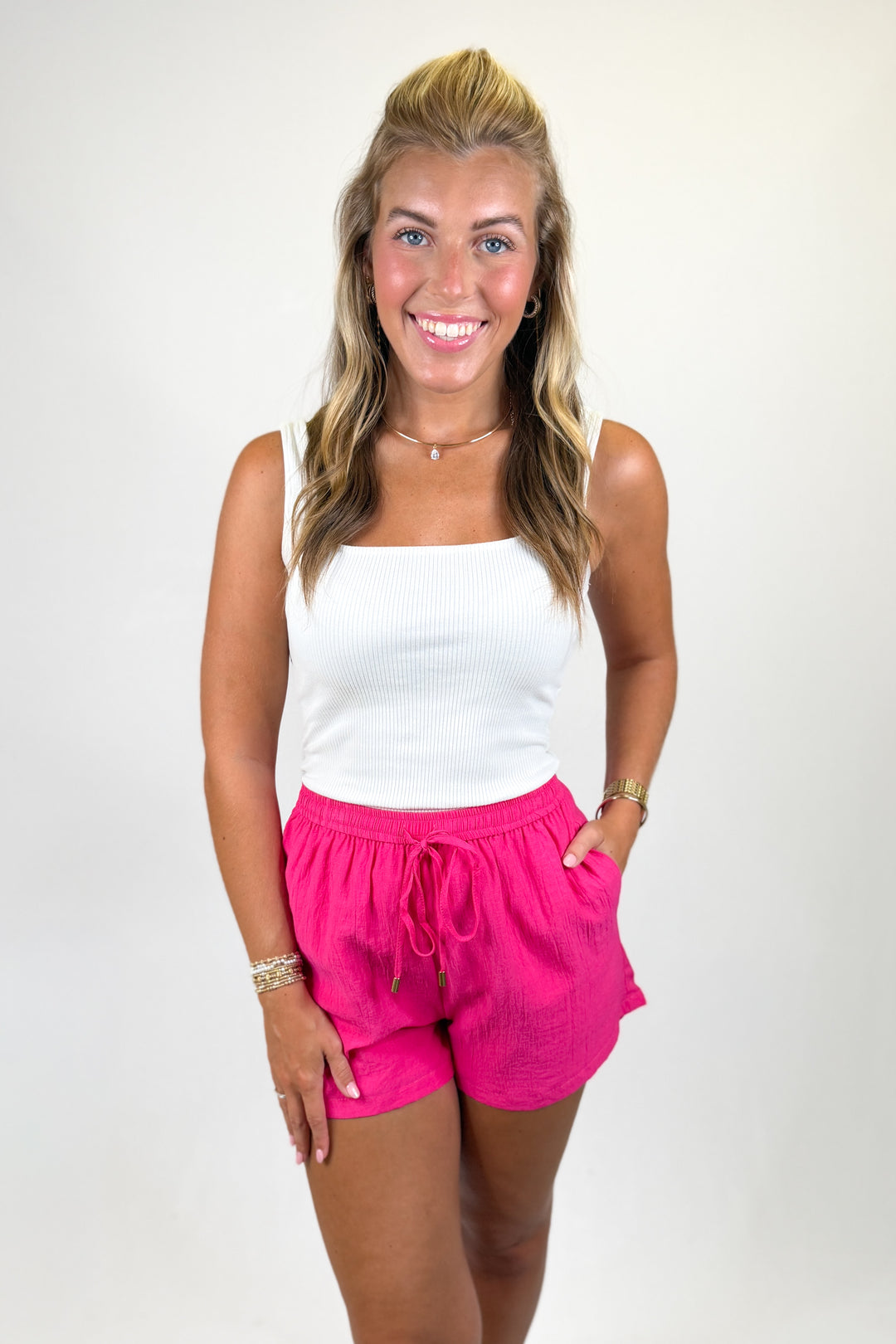 Woman wearing a white tank top and pink shorts on a plain background