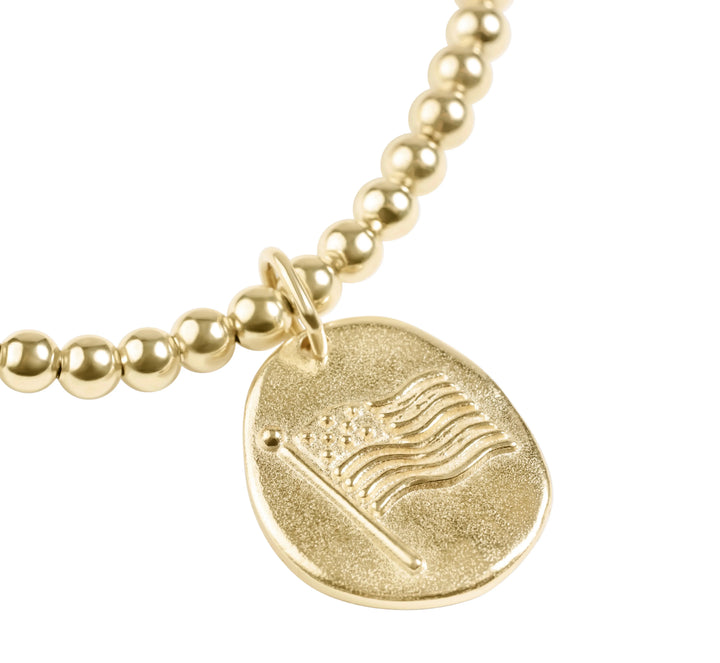 Gold beaded bracelet with a round pendant featuring an American flag design on a white background.