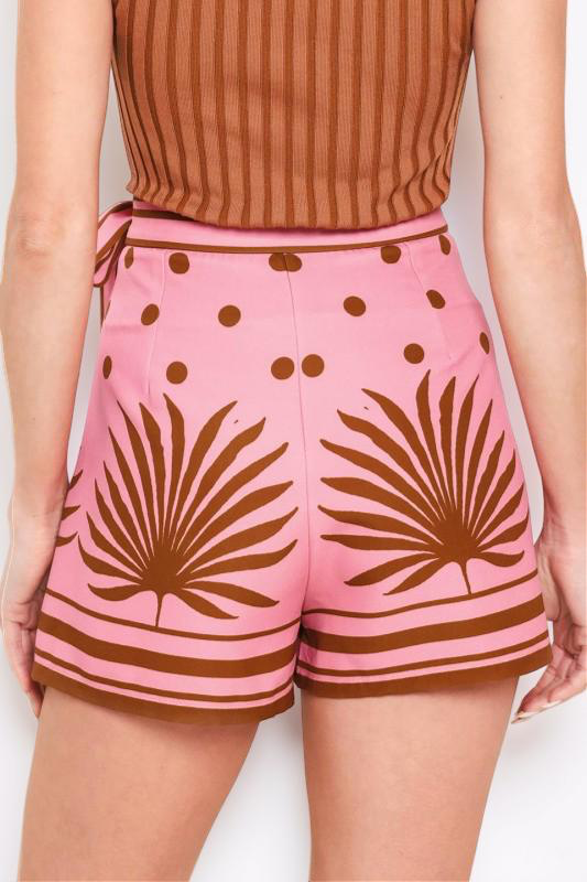 Person wearing pink shorts with brown leaf patterns and a brown top on a white background