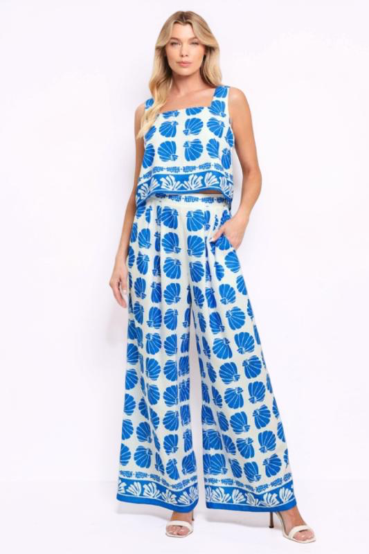 Woman wearing a blue and white shell pattern sleeveless top and wide-leg pants on a white background