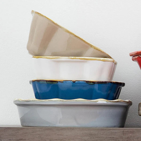 Stack of ceramic baking dishes in beige, blue, and gray on a white background