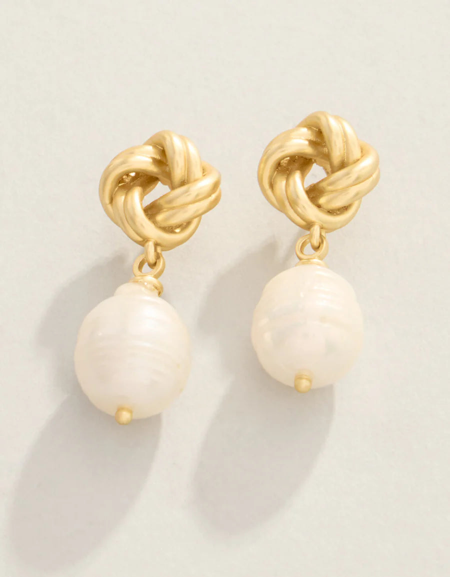 Gold earrings with white beads on a light background