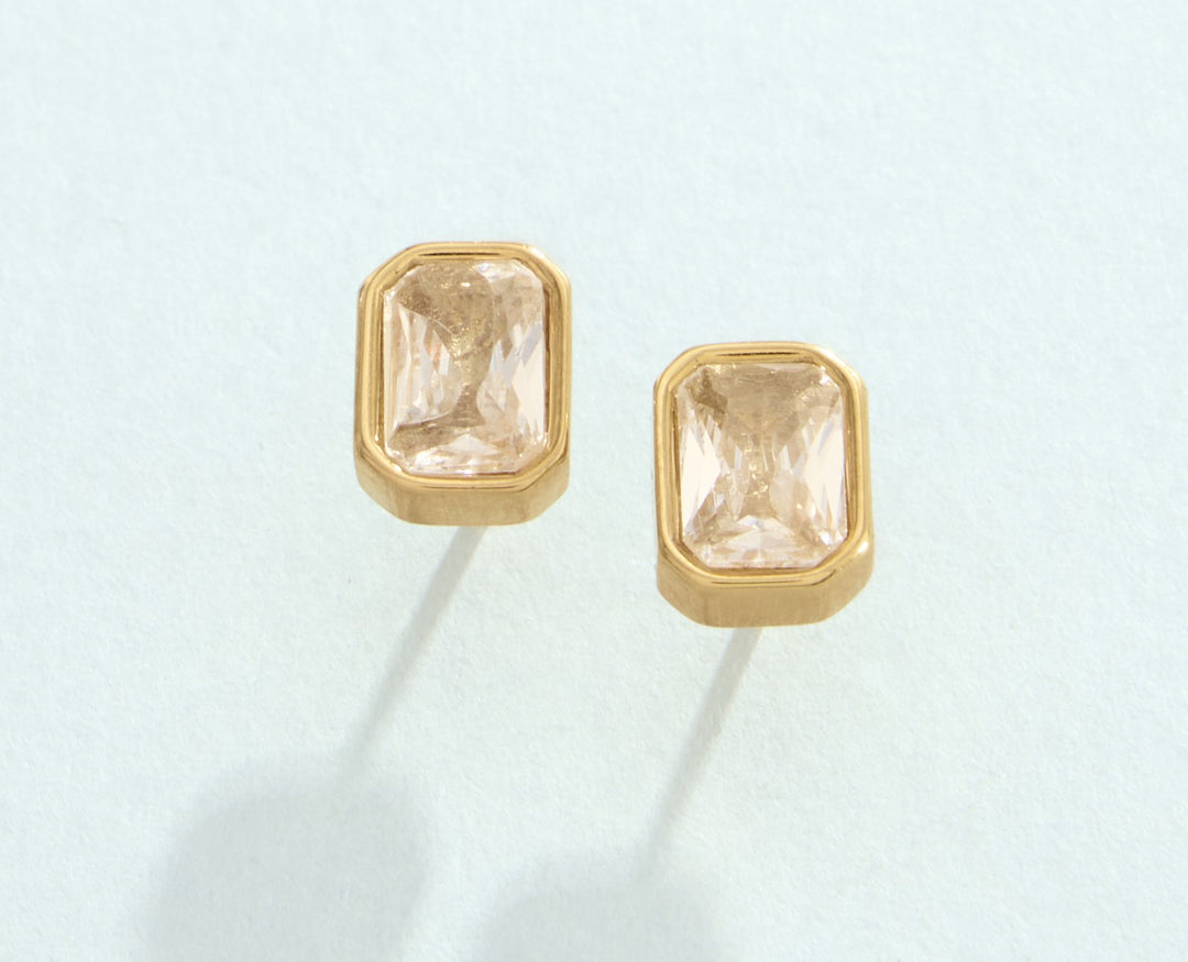 Gold earrings with rectangular gemstones on a light blue background