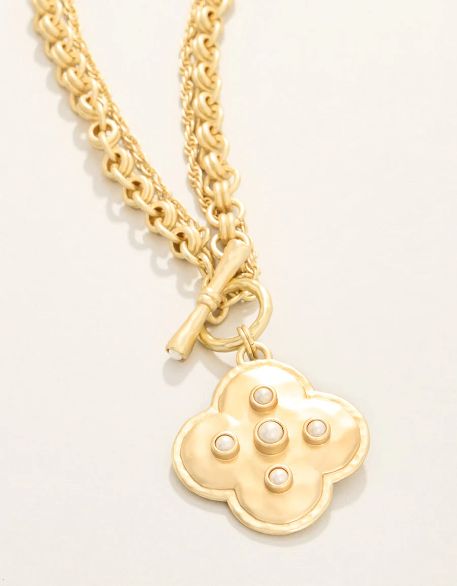 Gold necklace with a clover-shaped pendant on a light gray background
