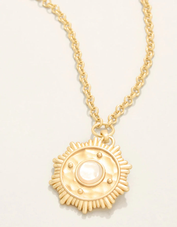 Gold necklace with a sun-shaped pendant on a light beige background