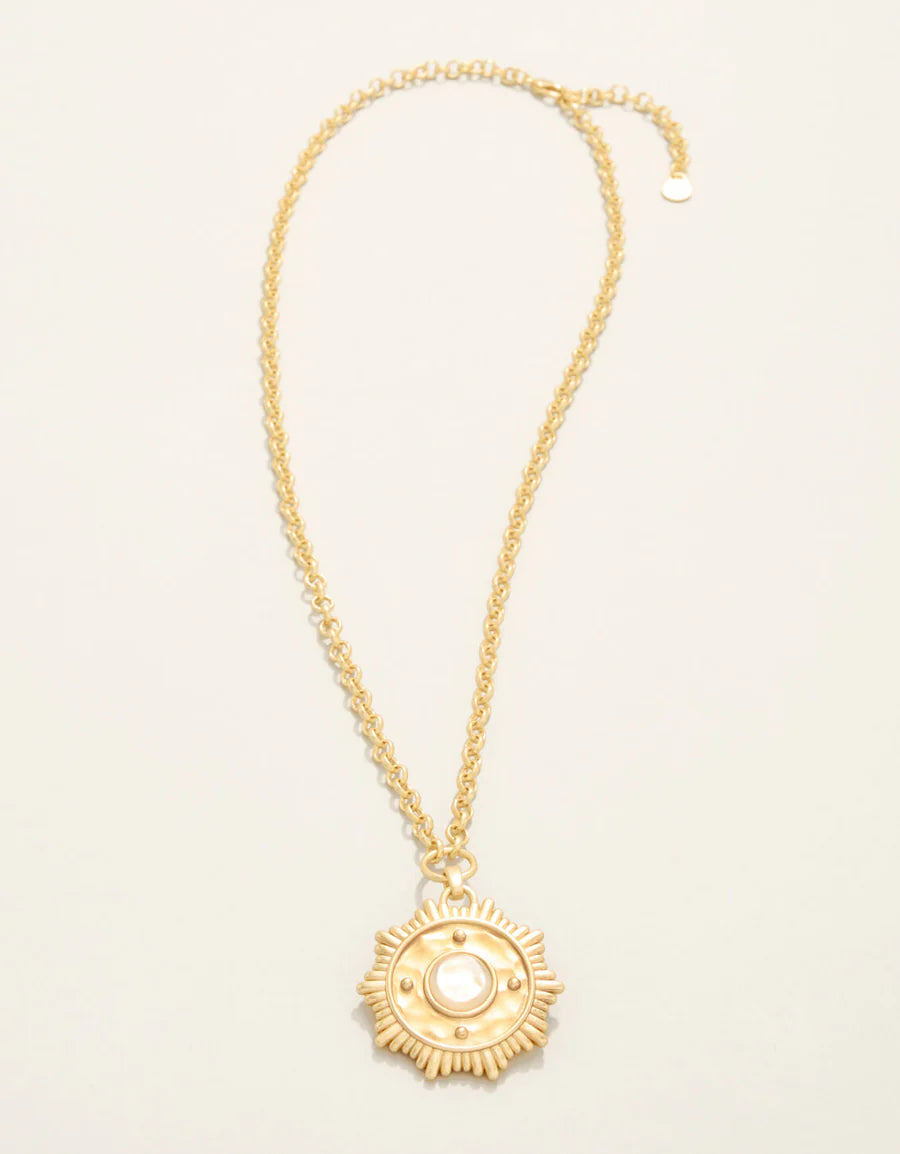 Gold necklace with a decorative pendant on a light beige background