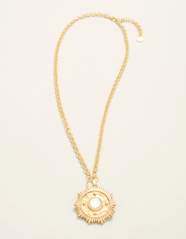 Gold necklace with a decorative pendant on a light beige background
