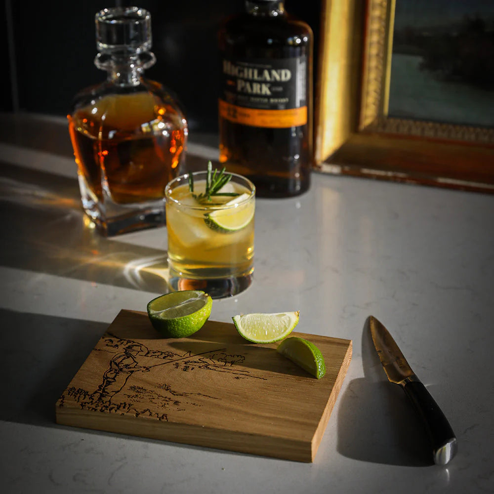 Cocktail with lime wedges on a wooden coaster, Highland Park whisky bottle in the background
