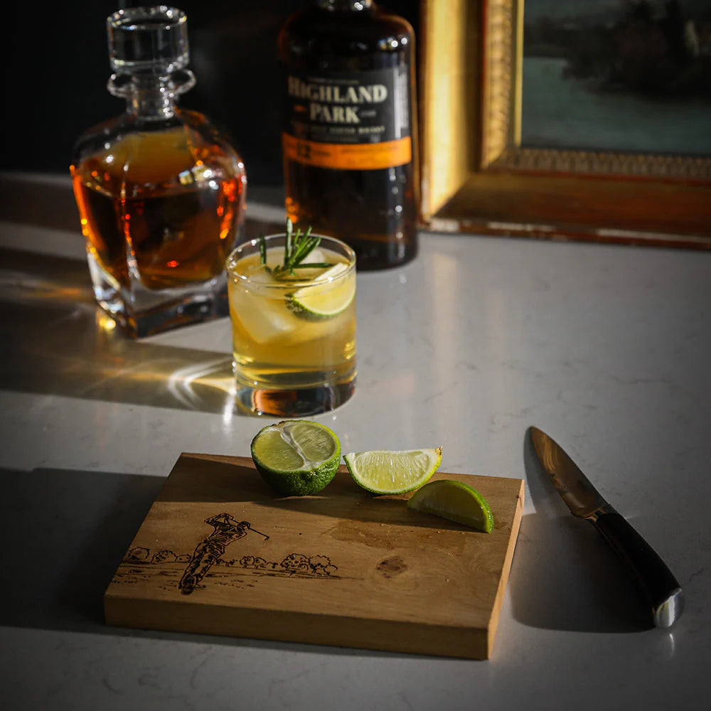 Cocktail with lime wedges on a wooden cutting board next to bottles of Highland Park whisky.