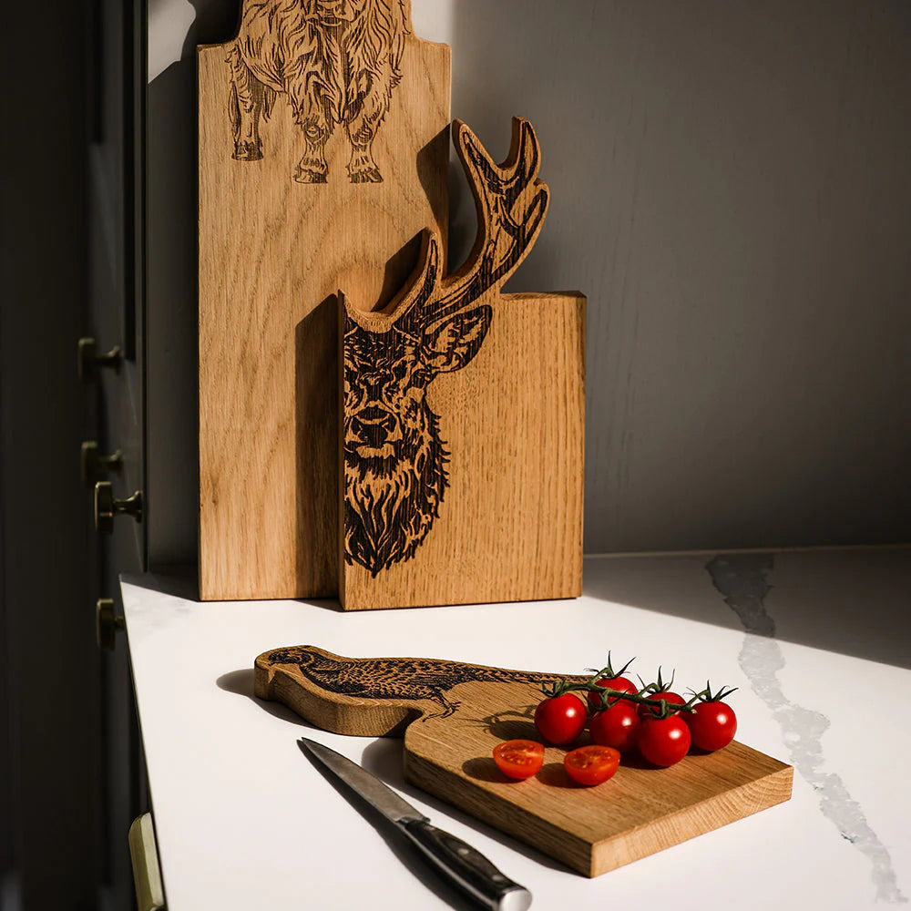 Wooden cutting board with deer design and tomatoes on a white surface