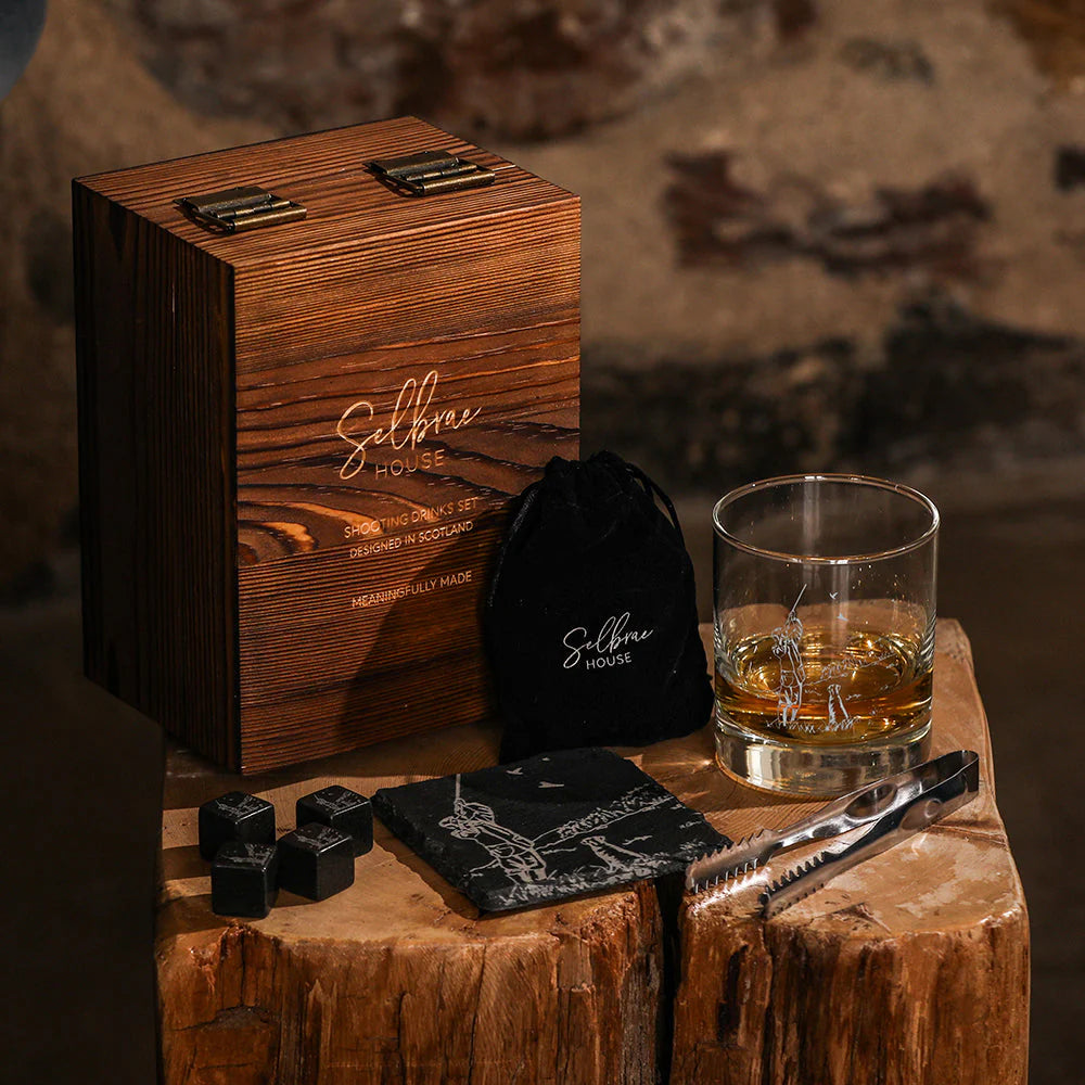 Wooden gift box with whiskey glass, coasters, and ice cubes on a wooden surface.
