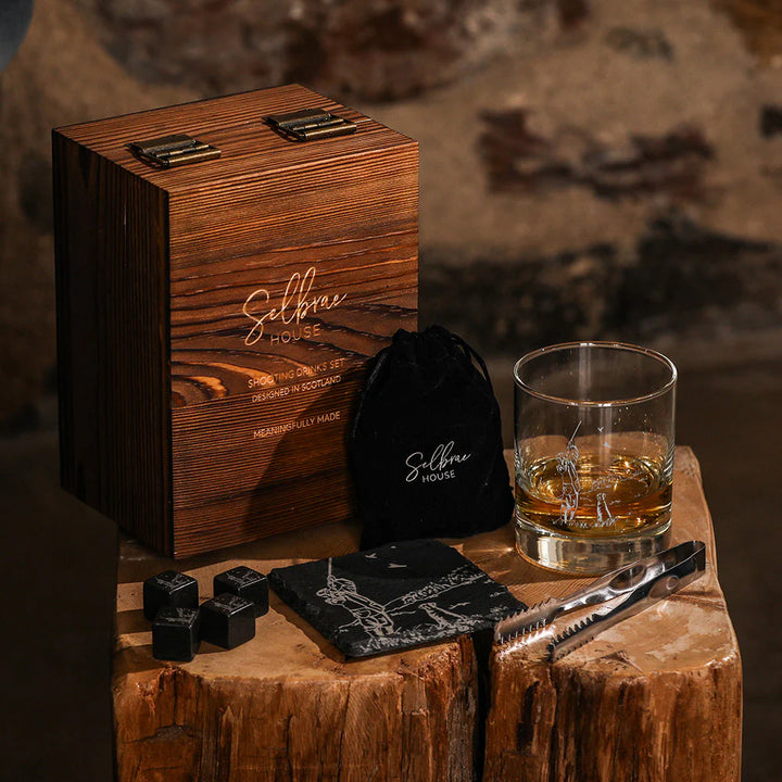 Wooden gift box with whiskey glass, coasters, and ice cubes on a wooden surface.
