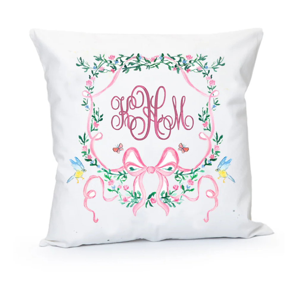 Decorative pillow with floral wreath and pink monogram on a white background