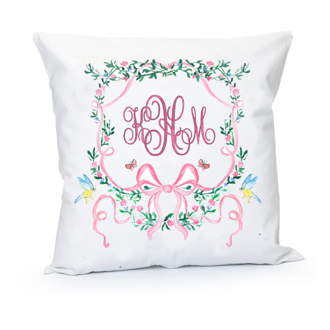Decorative pillow with floral wreath and pink monogram on a white background